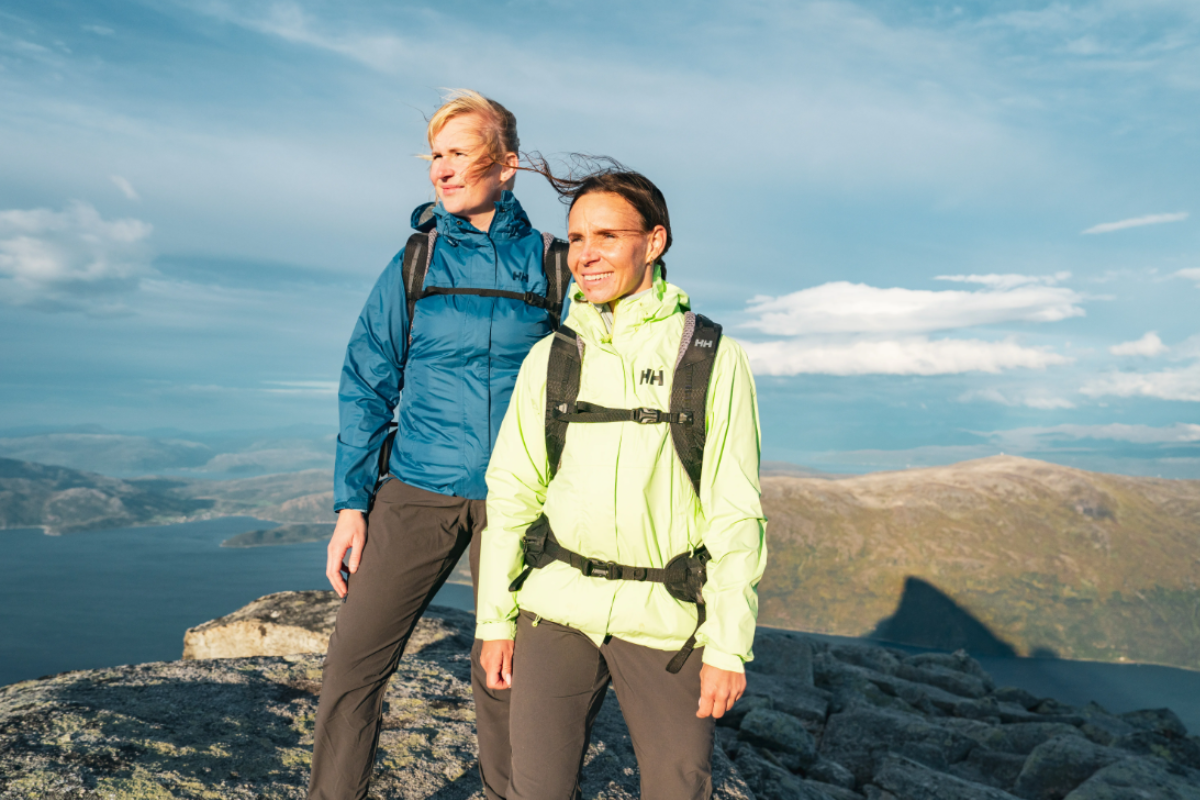 Две жени с планинска екипировка и раници Helly Hansen, застанали на скалист връх с панорамна гледка