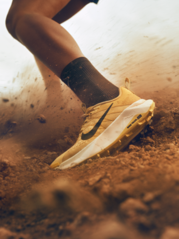 Жълта маратонка Nike Trail за планинско бягане в близък план, заснемаща момента на стъпване върху прашен и каменист терен.