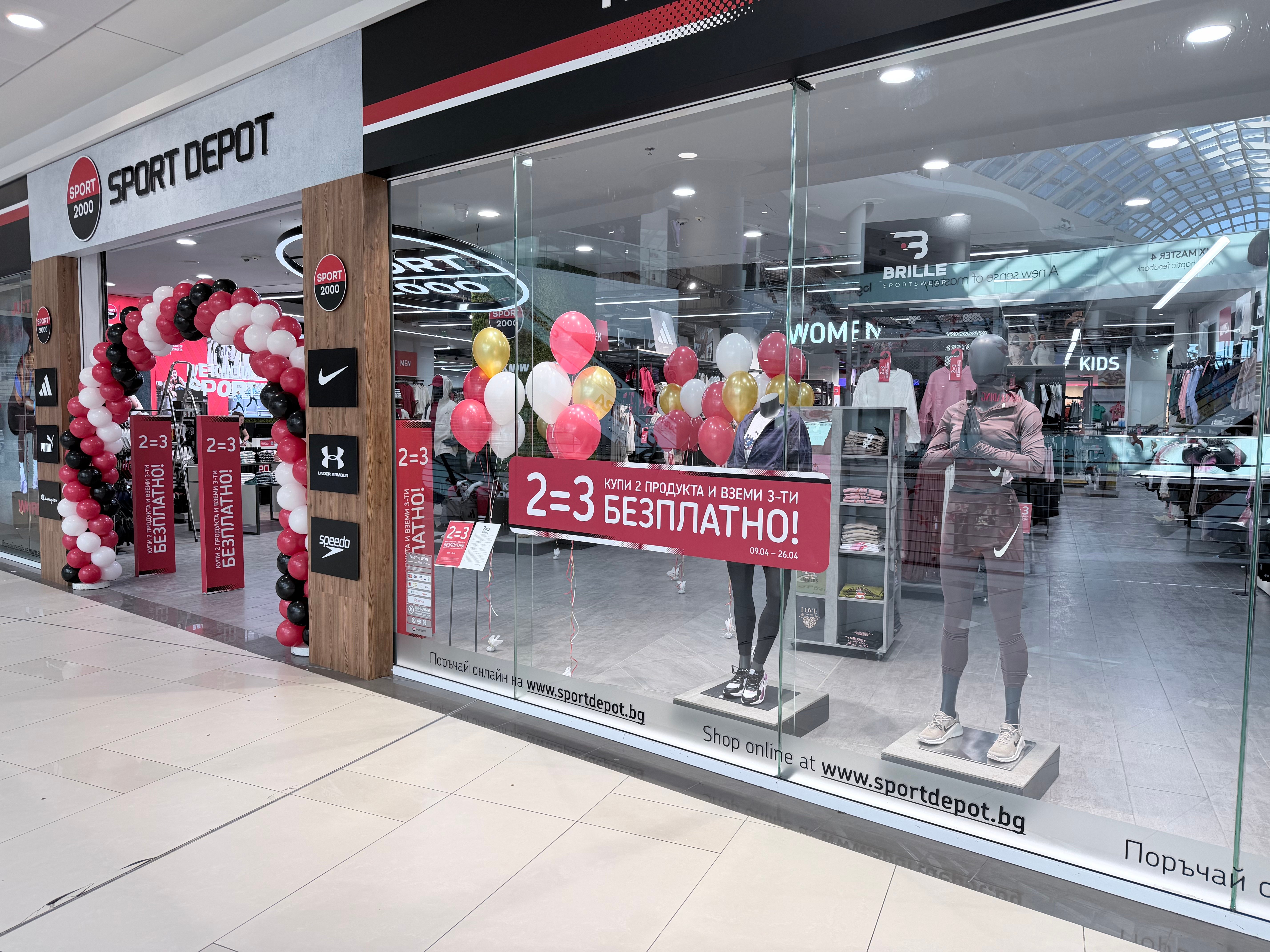 Витрина на магазин SPORT DEPOT с голям рекламен надпис за промоция &bdquo;2=3 Купи 2 продукта и вземи 3-тия БЕЗПЛАТНО&ldquo; и празнична декорация с балони.