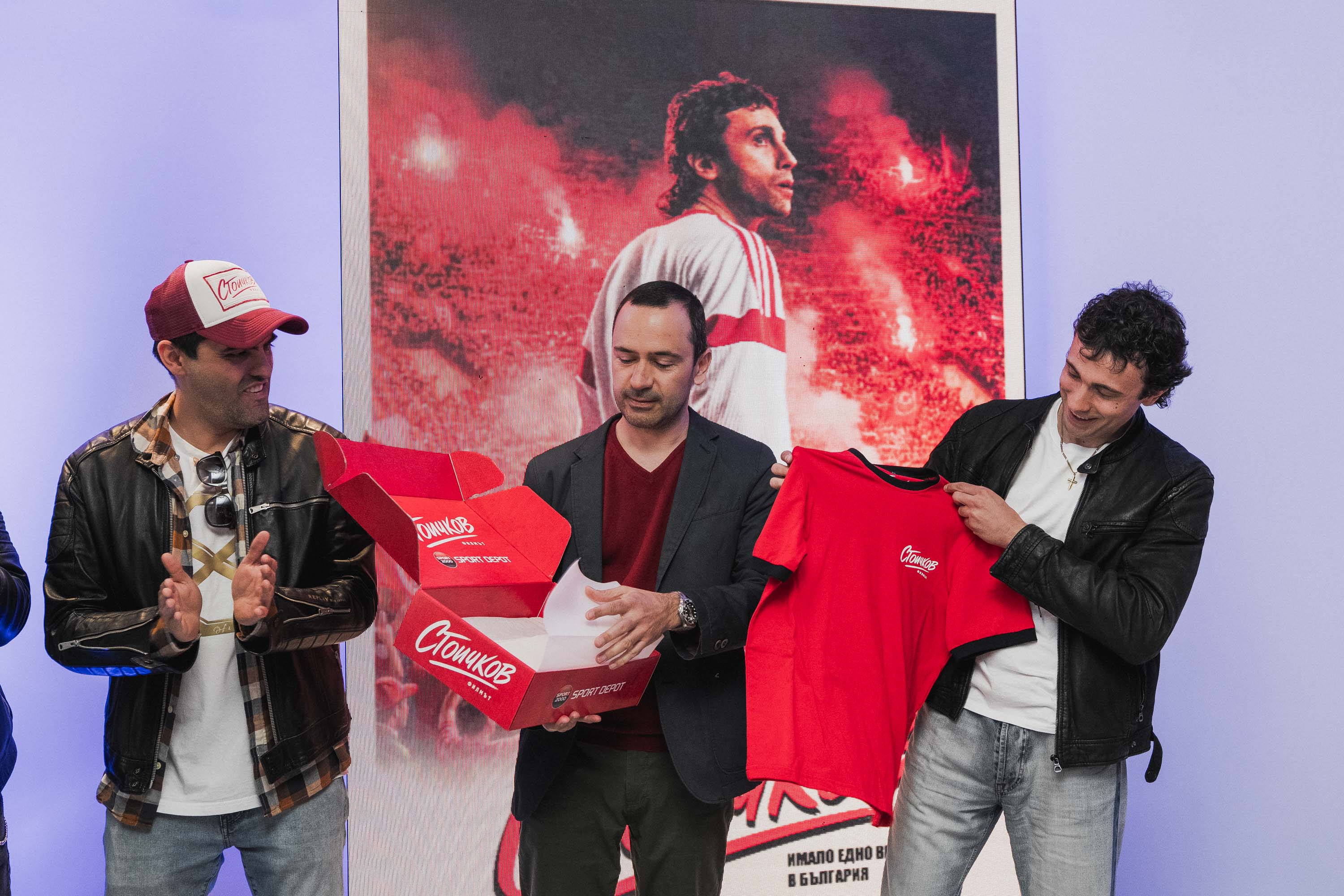 Николай Цонов от SPORT DEPOT представя съдържанието на специална кутия &bdquo;Стоичков&ldquo; на Александър Сано и актьорът Кристо Стоичков, който държи червена тениска с логото &bdquo;Стоичков&ldquo;