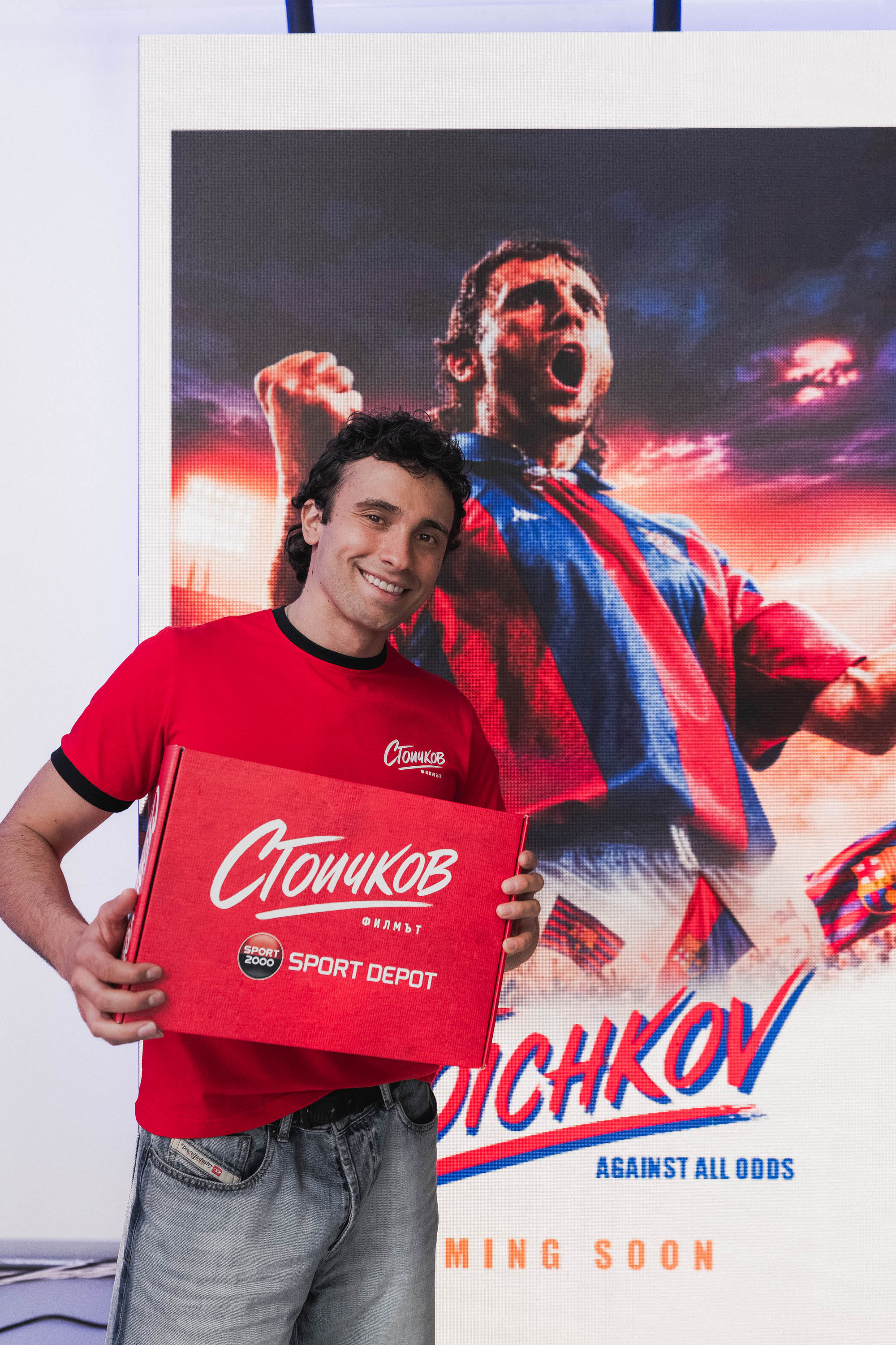 Актьорът Кристо Стоичков, който влиза в роклята на великият Христо Стоичков, държи брандирана червена кутия на SPORT DEPOT