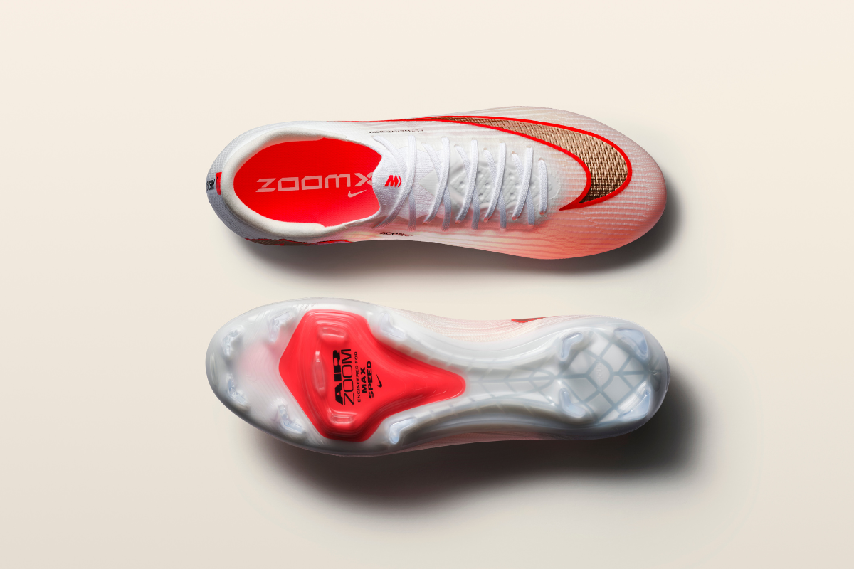 Изглед отгоре на бяла футболна обувка Nike Mercurial със златно лого и червена стелка ZoomX, заедно с изглед на подметката с прозрачна Air Zoom възглавница и шипове.