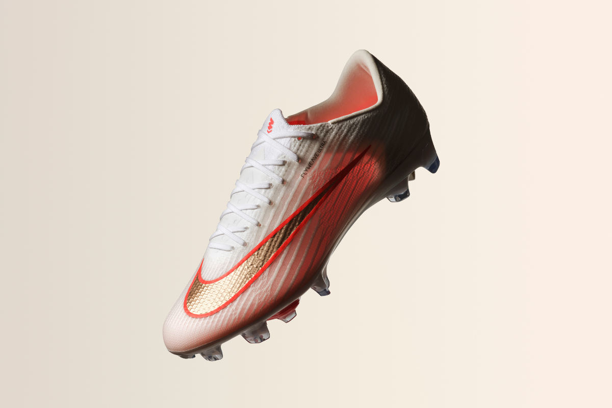 Страничен изглед на футболна бутонка Nike Mercurial Flyweave Ultra в бял цвят с червени акценти, златиста запетая отстрани и прозрачна подметка.