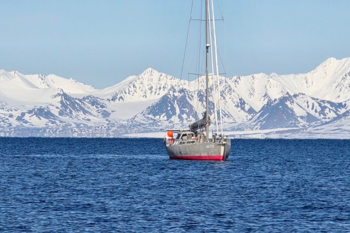 Ветроходната яхта на Mirabo Adventures плава в сините води на Антарктида на фона на величествени, заснежени планински върхове."