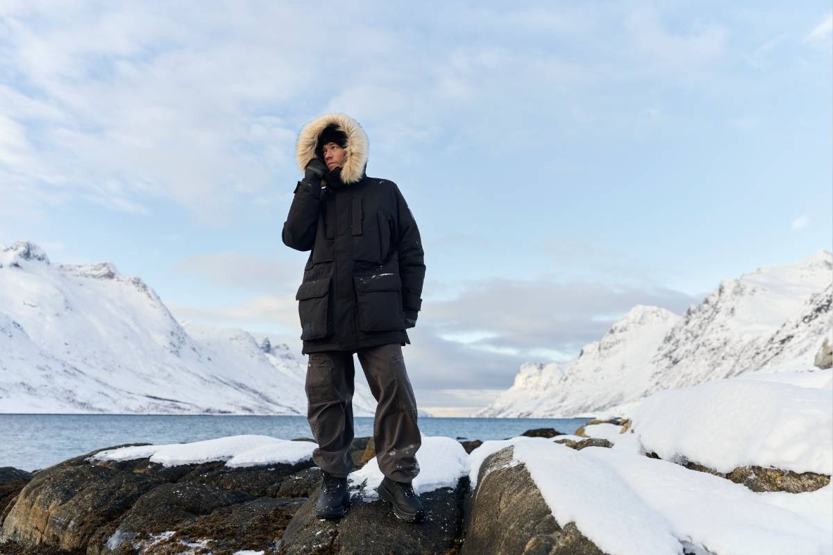 Мъж с черно зимно яке парка Helly Hansen outdoor - на фона на заснежена планина и езеро.
