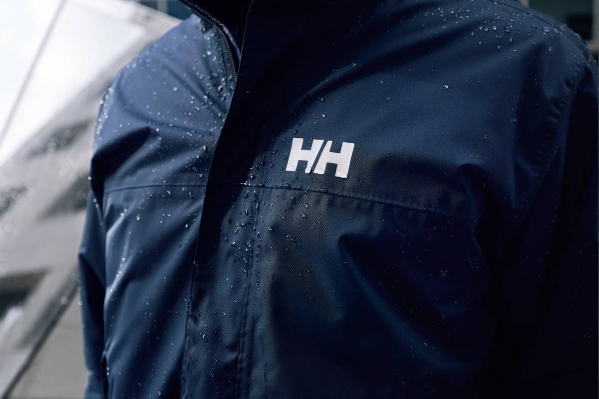 Близък план на водоустойчиво яке Helly Hansen с капки дъжд и логото HH.