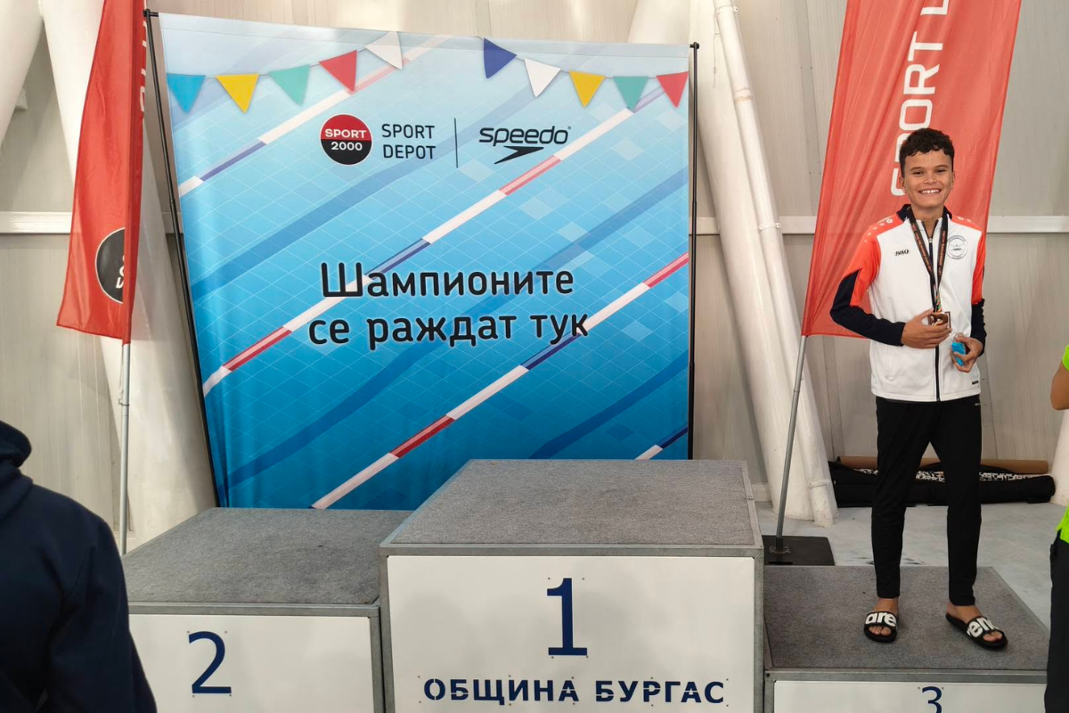 Млад плувец с медал на почетната стълбичка пред брандирана стена на SPORT DEPOT и Speedo на турнира по плуване „Бриз“.