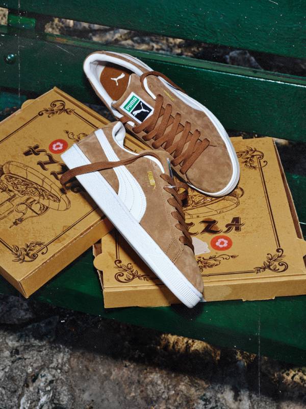 Кафeви велурени обувки Puma Suede Classic с бели ленти и подметка, поставени върху кутии от пица