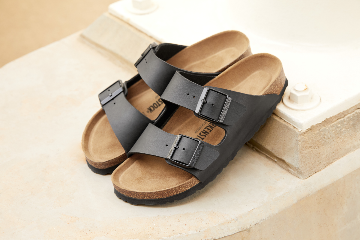 Черни сандали Birkenstock модел Arizona с две каишки, черни катарами и класическа коркова подметка, поставени на открито върху светла каменна повърхност.