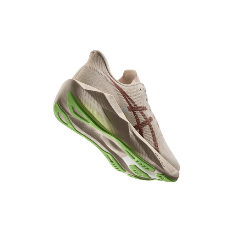 Снимка под ъгъл на маратонка Asics Novablast 6 в бежово и зелено, видяна отстрани и отдолу, показваща дебелата междинна подметка и яркозеления грайфер на подметката на бял фон.