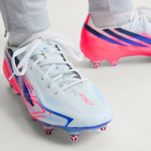 Близък план на бели футболни обувки adidas F50 Hyperfast Elite SG с бутони за мокър и кален терен от естествена трева 