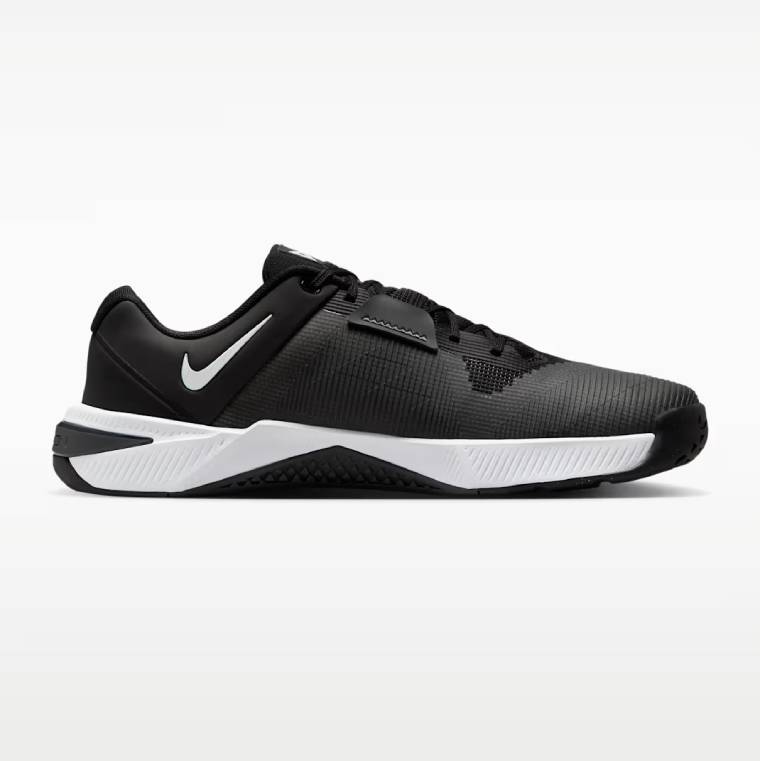 Профилен изглед на обувка за тренировки Nike Metcon 10. Обувката е с черно-бяла основа, дишаща мрежа в черен цвят, бяло лого Nike при петата и здрава подметка.
