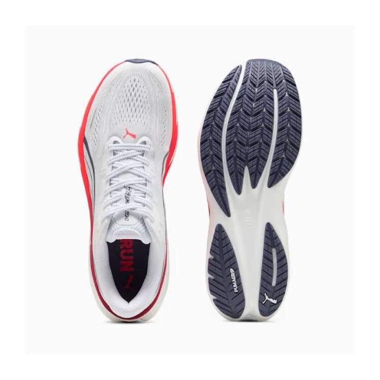 Изглед отгоре на бяла маратонка Puma Velocity Nitro 5 с червено-оранжеви акценти, показана до тъмносивата си грайферна подметка PUMAGRIP. 